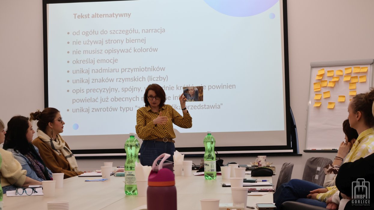 Biblioteka Gorlice, Szkolenie o odstępności prowadząca na tle ekranu pokazuje uczestnikom fotografię